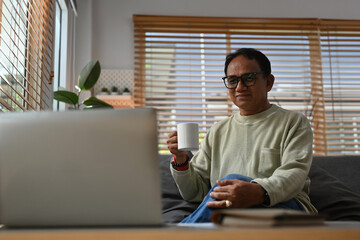 Portrait with middle aged Asian man looking at laptop during sitting on the sofa and enjoy with coffee drink.