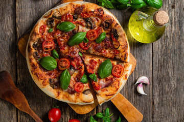 Appetizing pizza. Pizza with ham, mushrooms and tomatoes on a wooden background
