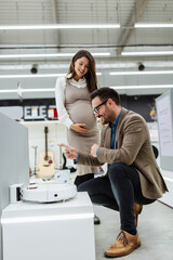 Beautiful and happy middle age couple buying consumer tech products in modern home tech store. They are choosing and trying robot vacuum or mop. People and consumerism concept.