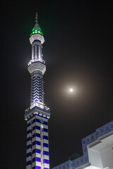 Blue and white minaret of the mosque in the night with moon on the sky