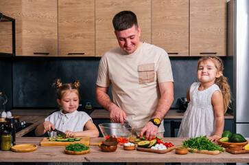 Young father cooking with his little daughters. Father teaching kids how yo cook.