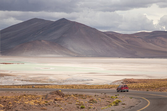 A red car on road at Piedras rojas in Atacama desert, colorful landscapes of a Salt Flat and the altiplano lakes with black volcanos at the background, situated in the heart of the Chilean altiplano