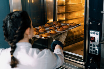 attractive baker takes ready buns and croissants from professional oven bakery production fresh...