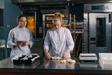 two bakers shape the raw dough before baking, cut it and roll it out on the table professional kitchen bakery pastry production