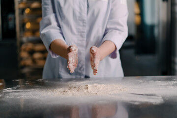 An experienced chef applies flour to his hands before making bread in a bakery prepares pastries in a professional kitchen