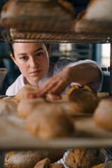 Obraz na płótnie Canvas attractive female baker between shelves looking and checking freshly baked bread very carefully in bakery industry