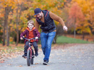Father teaching his little son to ride bicycle in park. Bearded man running and holding childs bike. Family values, child support, fathers day concept. Selective focus.