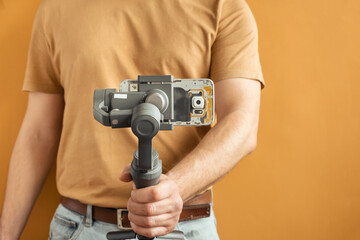 Man filming with a smartphone using a gimbal stabilizer on yellow background. Using three-axis...