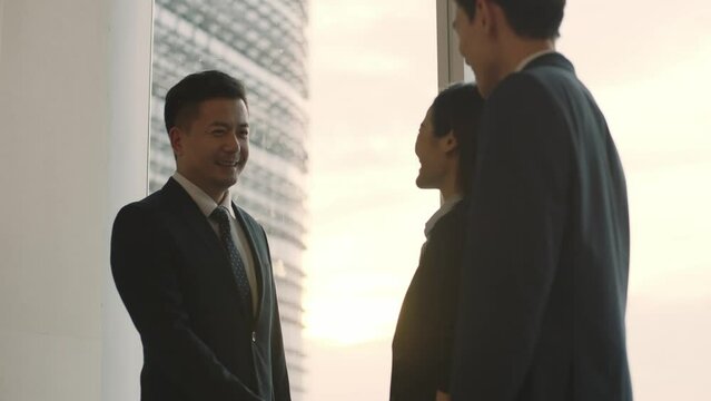 asian business man standing by the window in office shaking hands and chatting with visiting clients