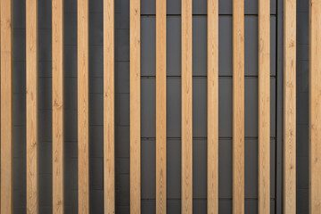 Close-up of modern façade made of untreated larchwood strips in front of dark sheet metal façade panels and concrete blocks