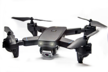 A small dark gray quadrocopter on a white background with glowing headlights and glare close-up	
