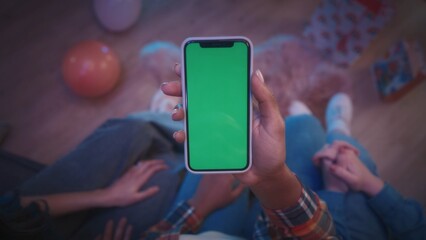 Hands of an African American woman holding a phone with a green screen close up on her knees. The girl at the party shows her friends on the phone a photo, video.
