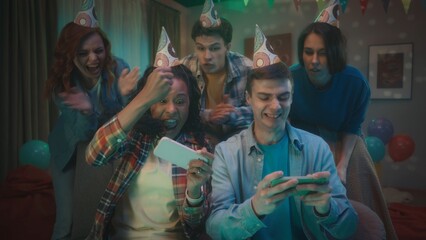 An African American girl and a Caucasian man are playing an online game on their phones, they are supported by friends standing behind their backs. The girl wins, makes a victory gesture with her hand