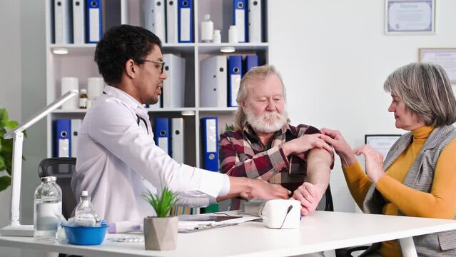 health care, young afro american male doctor measures blood pressure to elderly man together with old wife in doctor's office