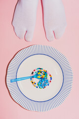 Feet in white tabi socks stand near colored necklaces with beads in the form of food on a plate on pink background. Creative concept, flat lay, top view - 606503317