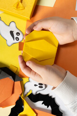 Origami crafts for Halloween - pumpkin made of paper in the hands of a child, top view.