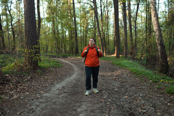 Fototapeta premium Traveling woman with backpack walking through a spring green forest at sunny day. High quality photo