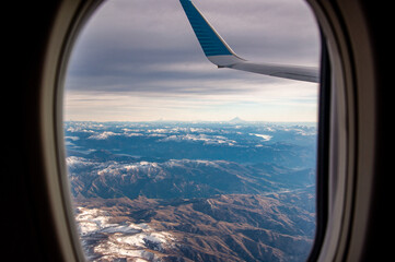 View of the snow covered Andes Mountains through the window of an airplane at sunrise