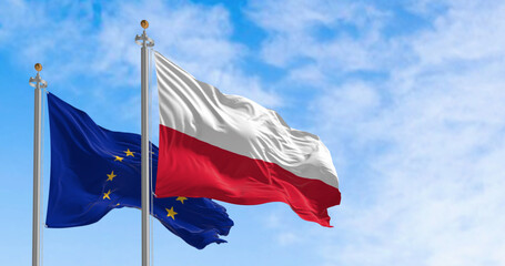 The flags of the Poland and the European Union waving in the wind on a clear day