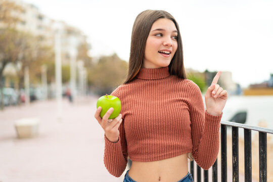 Teenager girl with an apple at outdoors intending to realizes the solution while lifting a finger up