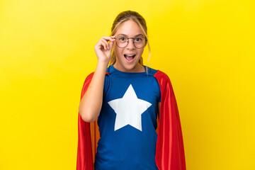 Super Hero little girl isolated on yellow background with glasses and surprised