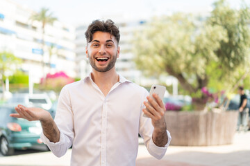Young handsome man using mobile phone at outdoors with shocked facial expression