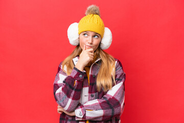 Young beautiful woman wearing winter muffs isolated on red background having doubts and with confuse face expression