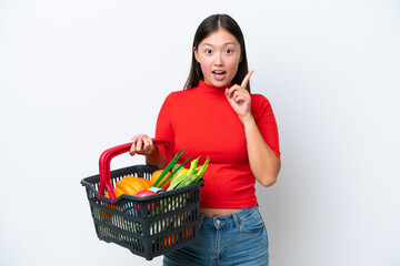 Obraz na płótnie Canvas Young Asian woman holding a shopping basket full of food isolated on white background intending to realizes the solution while lifting a finger up
