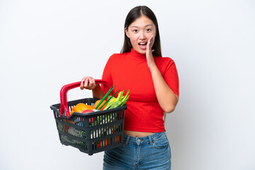 Fototapeta na wymiar Young Asian woman holding a shopping basket full of food isolated on white background with surprise and shocked facial expression