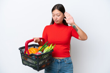 Fototapeta na wymiar Young Asian woman holding a shopping basket full of food isolated on white background making stop gesture and disappointed