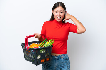 Fototapeta na wymiar Young Asian woman holding a shopping basket full of food isolated on white background making phone gesture. Call me back sign