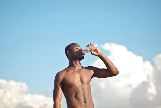 young shirtless man drinks from a plastic bottle