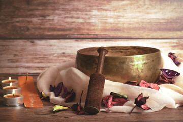 tibetan bowl with incense, lighted candles and colorful flower petals on a wooden table and copy...