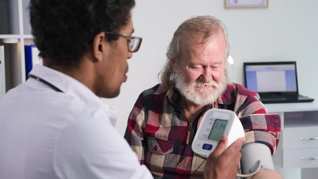 modern medical equipment, a young professional black doctor measures pressure of an elderly man during a medical examination in office