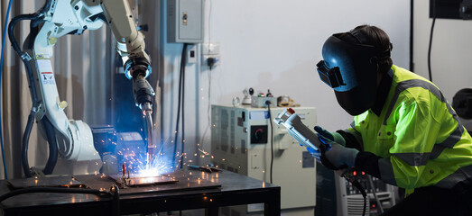 Male engineer working control robot arm system welding with welding protective mask at production...