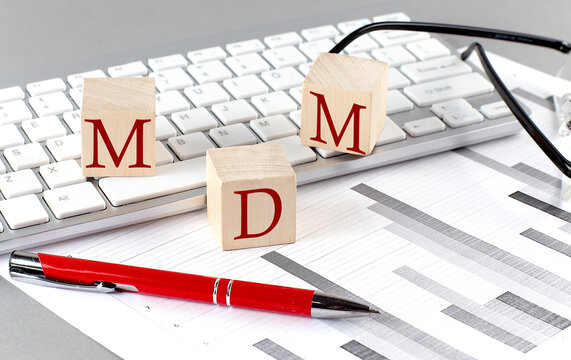 MDM written on a wooden cube on the keyboard with chart on grey background