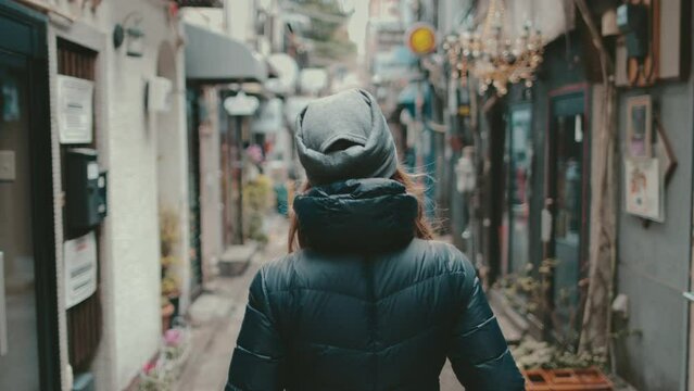 Woman tourist walking small city street in Tokyo. Caucasian girl enjoy backstreet alley with old restaurants, pubs, drinking bars. Golden Gai Street, Japanese. Back view slow motion. Travel, tourism