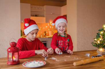 A cute little girl and boy in a Christmas cap make gingerbread cookies in the New Year's kitchen.