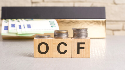 wooden blocks with letters OCF - acronym from Operating Cash Flow, a box of euro bills in the background