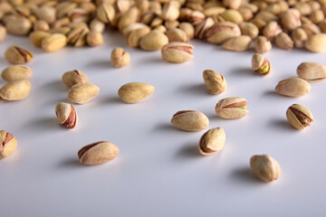 A lot of healthy, delicious, high-calorie, nutritious pistachio nuts in a hard yellow shell are scattered on a white background. Roasted pistachios in the shell on the background of a white table