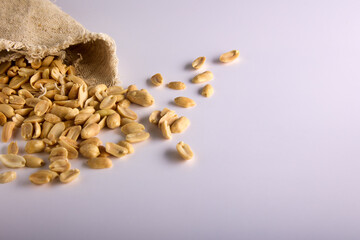 Lots of roasted delicious peanuts scattered on a white background from an open storage bag. Salted...