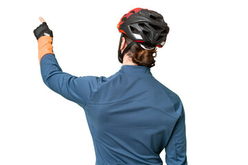 Young cyclist man over isolated chroma key background pointing back with the index finger