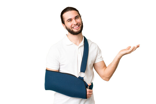 Young handsome man with broken arm and wearing a sling over isolated chroma key background extending hands to the side for inviting to come