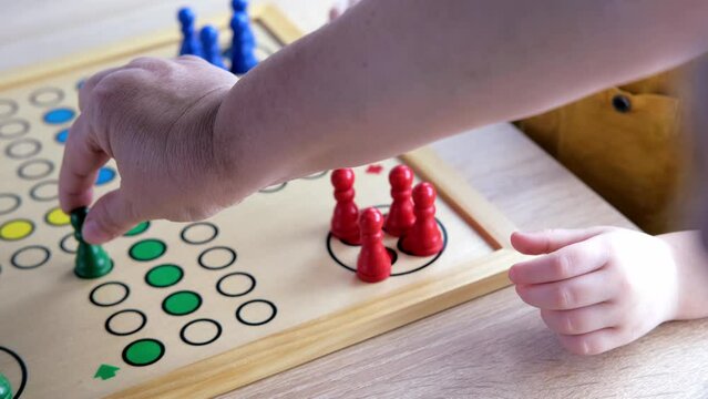 close-up of hands of small child manipulate with wooden figurines of family board game, smart kid, 2-year-old girl is learning to count, Cross and circle game Parcheesi, foreground focus