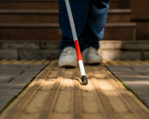 A blind woman walks outdoors using a cane along a tactile yellow tile.