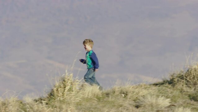 Cute 4 year old boy in sweater runs down hill, filmed with 800mm telephoto