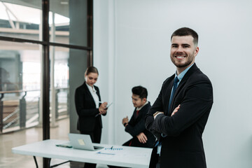 Handsome businessman standing confidently with arms crossed in office in front of his team