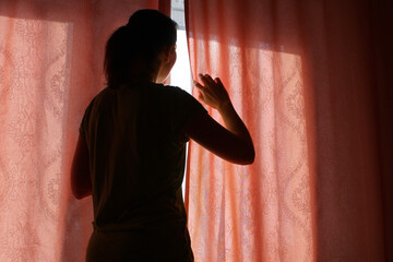 the woman behind the curtain cautiously looks out of the window into the street.