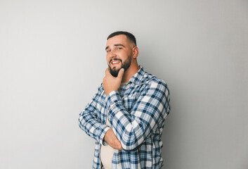 A young handsome guy in a plaid shirt holds his hand on his chin and looks thoughtfully into the camera, isolated on a gray background. young man comes up with an idea