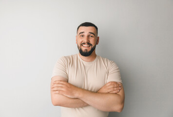 Confident young handsome man in shirt keeping arms crossed and smiling while standing against gray background